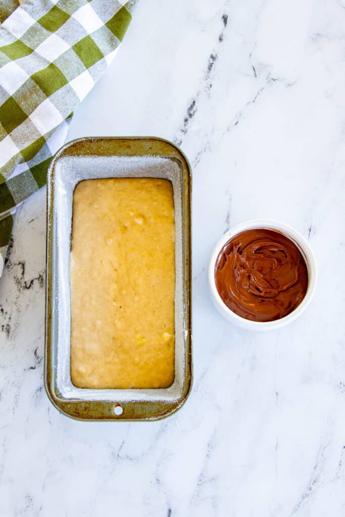 batter in a loaf pan with cup of Nutella spread on the side