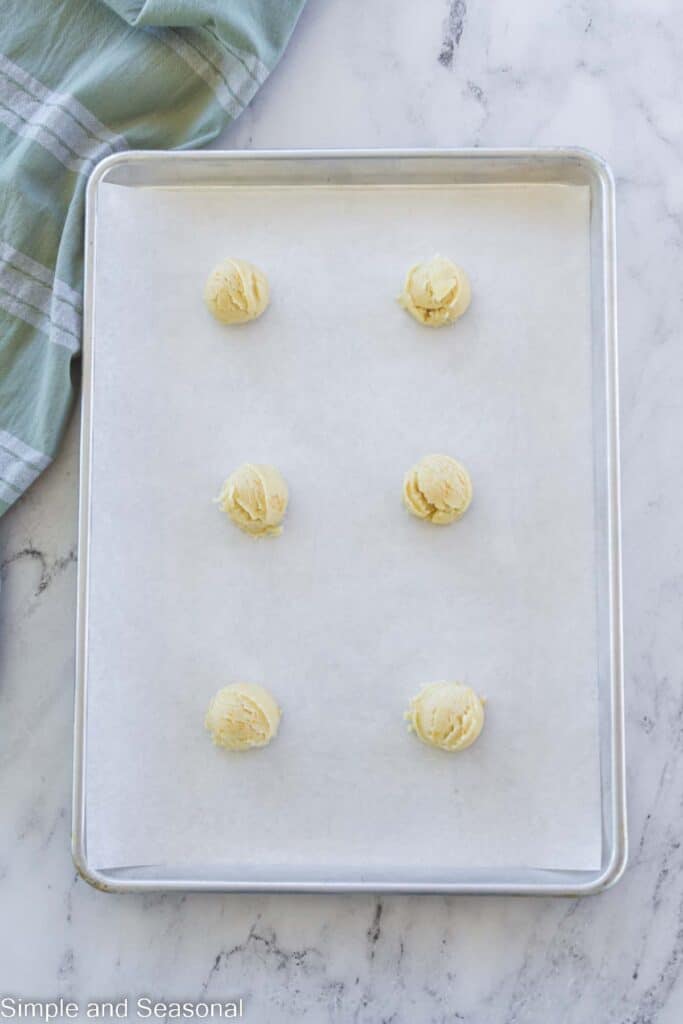 6 cookie dough balls on a parchment lined cookie sheet