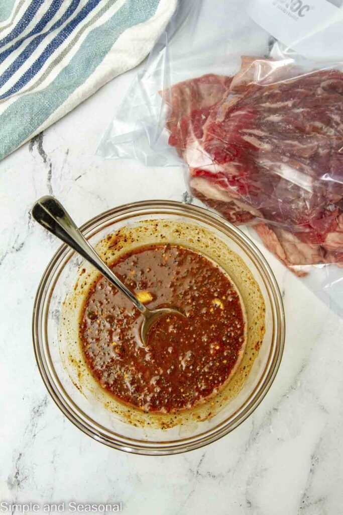 marinade for beef in a clear bowl and flank steak in a plastic bag