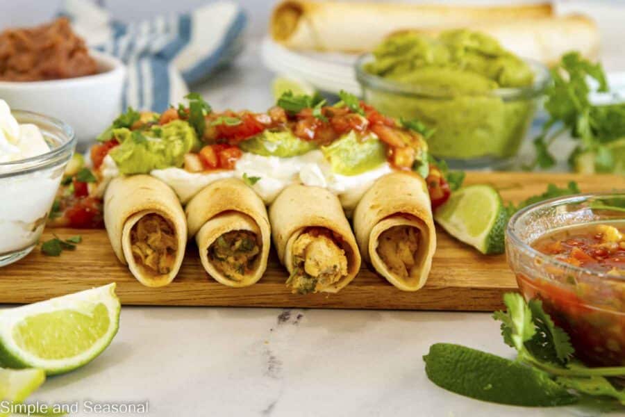 Closeup of side by side chicken taquitos with toppings on a platter