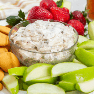 bowl of creamy dip with toffee bits surrounded by fruit and cookies