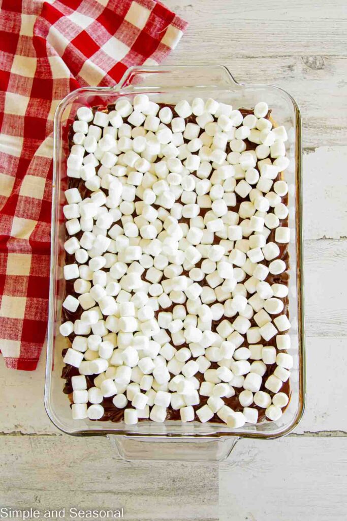 marshmallows placed on top of melted chocolate and cookie bar layers