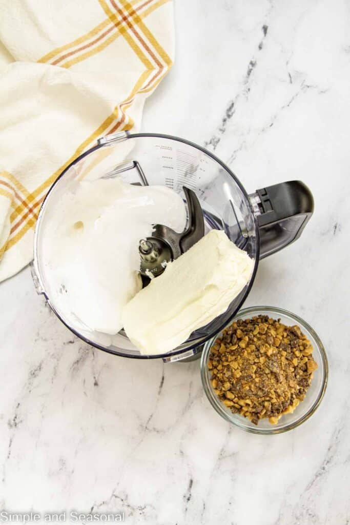 marshmallow fluff and cream cheese in a blender with a bowl of toffee bits on the side