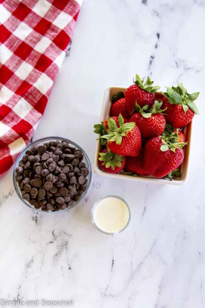 carton of strawberries, bowl of chocolate chips and small bowl of heavy cream