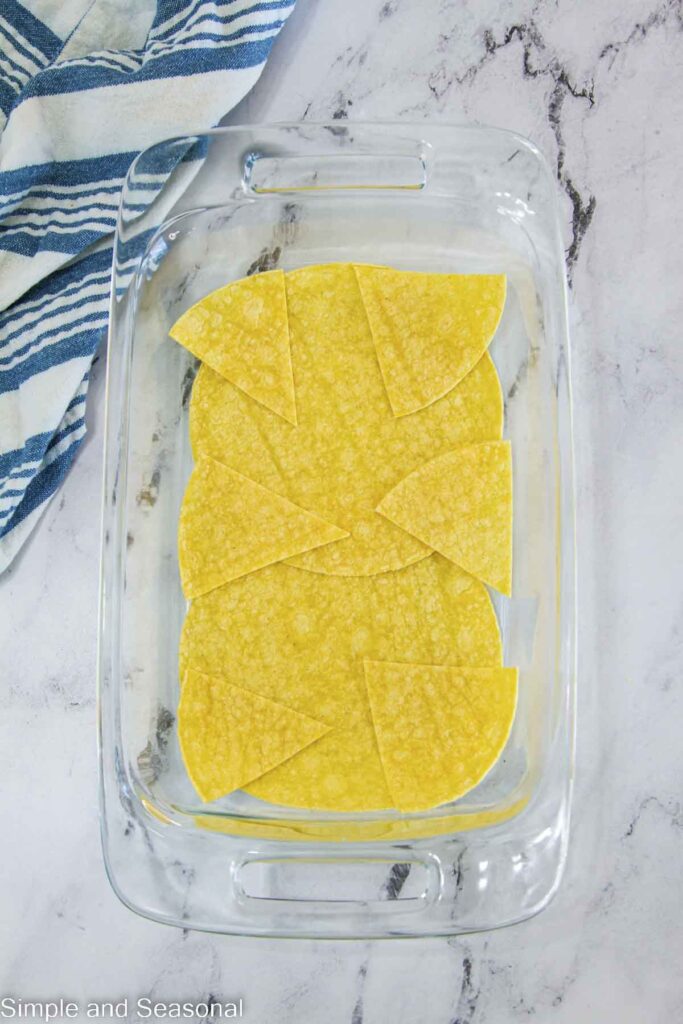 corn tortilla pieces in the bottom of a glass casserole dish