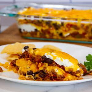 close up of tex mex casserole and tortilla chips on a plate with casserole in the background