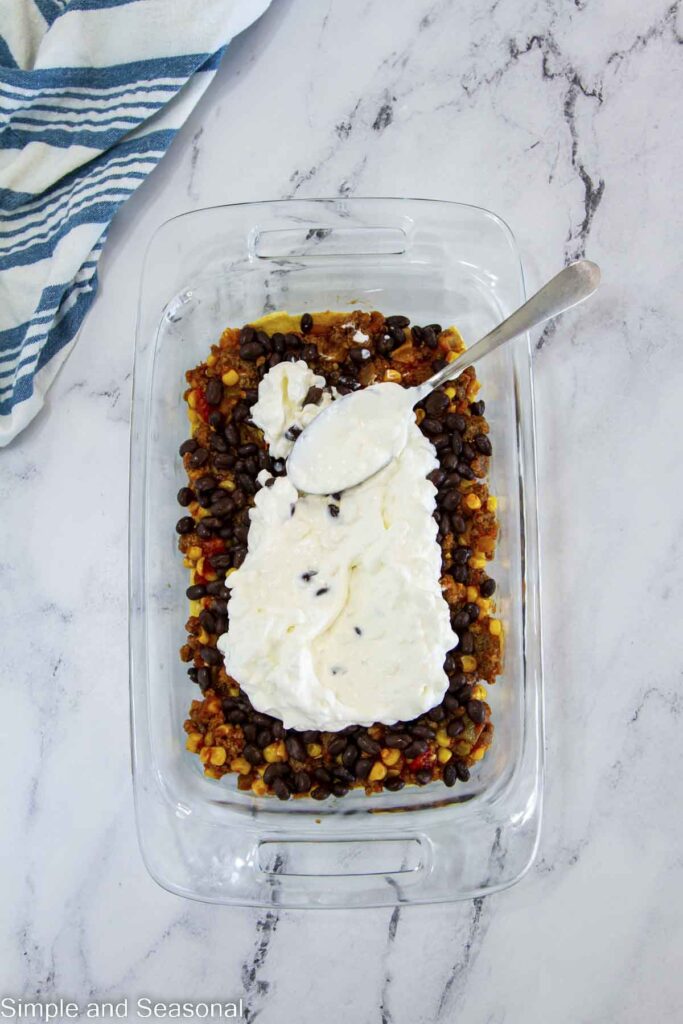 spoon spreading cream mixture over the layer of black beans