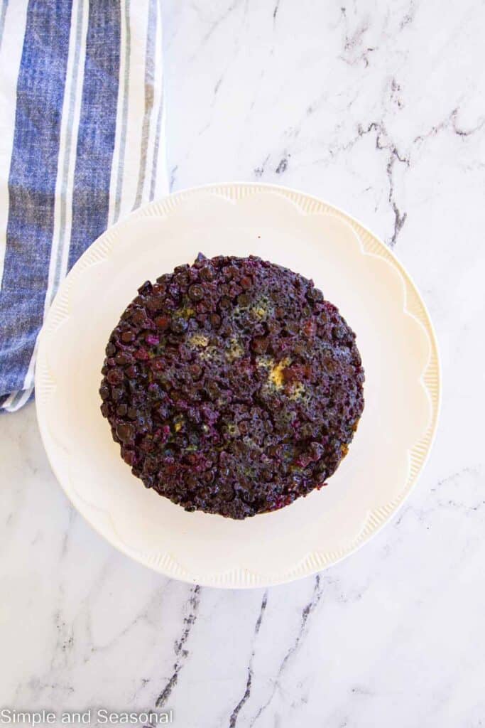 baked cake flipped over onto a cake plate-blueberry layer on top