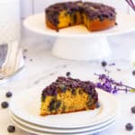 slice of cake on a plate with whole round cake on a platter in the background