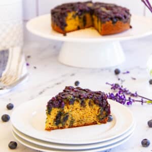 slice of cake on a plate with whole round cake on a platter in the background