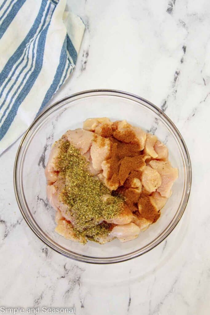 seasoning and raw chicken in a glass bowl