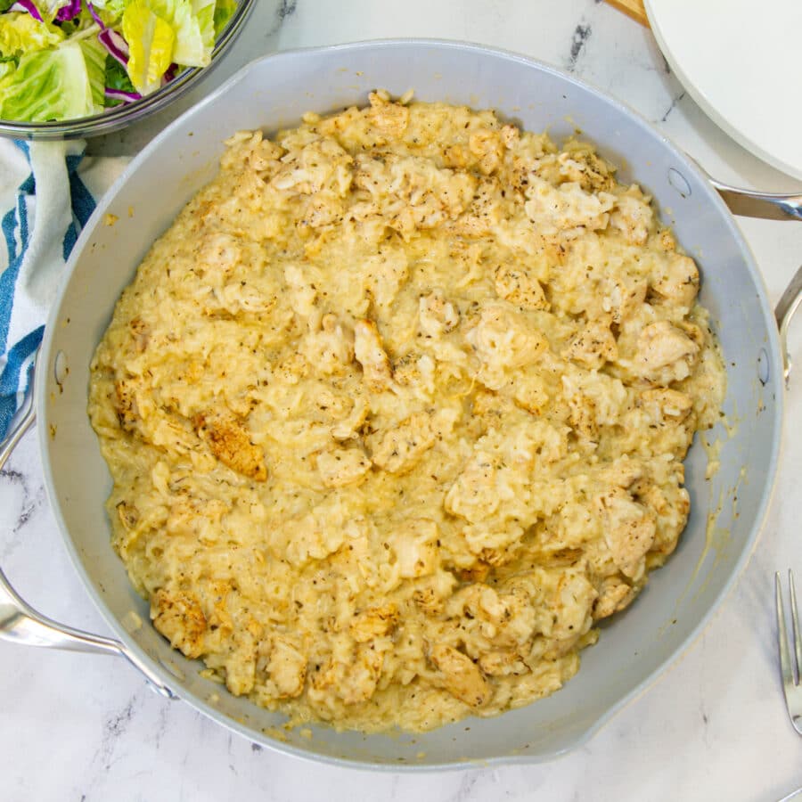 chicken and rice in the skillet with a salad on the side and a blue and while linen napkin