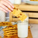 child's hand holding cookie stick over glass of milk
