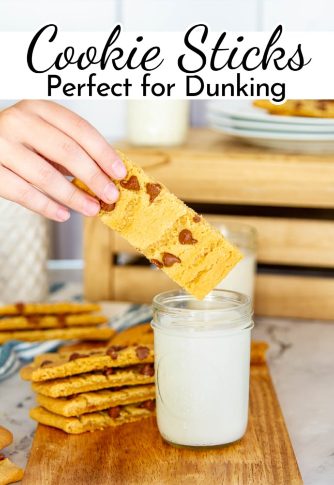 hand holding a chocolate chip cookie stick about to dunk it in a glass of milk