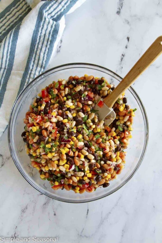 bean salad mixed together in a mixing bowl with spatula and linen napkin on the side